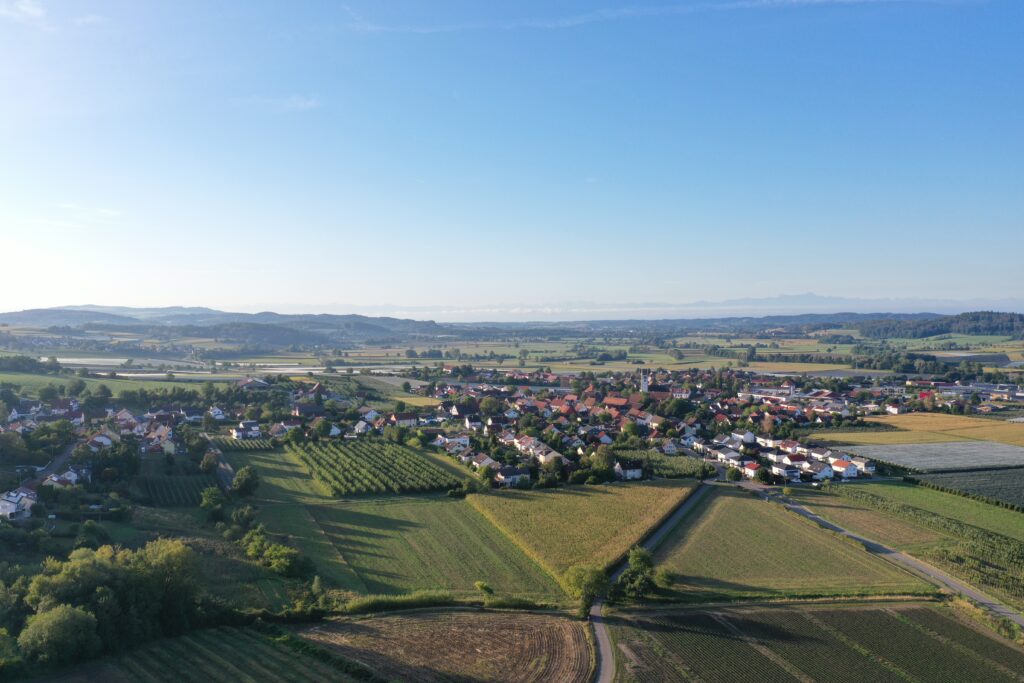 Luftbild von Frickingen im Linzgau zwischen Salemertal und Bodensee: Wohngebiete, Streuobstwiesen und Felder mit Alpenpanorama am Horizont.