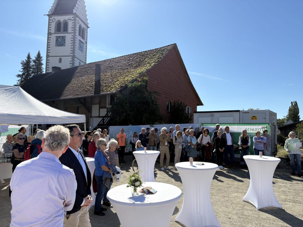 Gäste beim Spatenstich des LinzgAuDuo in Frickingen, im Hintergrund der Kirchturm und ein historischer Zehntscheuer-Bau.